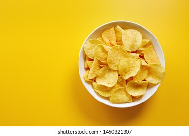 Close-up of potato chips or crisps in bowl against yellow background - Shutterstock ID 1450321307