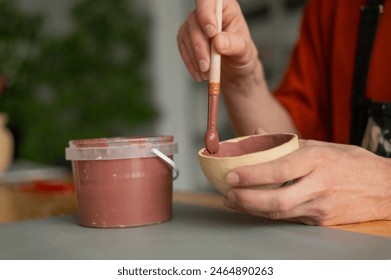 Close-up of a potter's hands with a brush painting ceramic dishes.  - Powered by Shutterstock