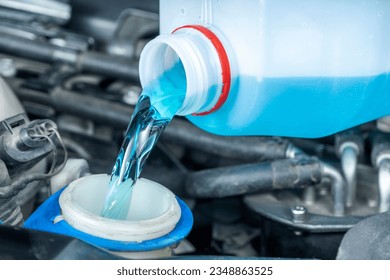 Close-up of pouring coolant or windshield wiper fluid from bottle to reservoir. Checks levels and periodic maintenance of cars in workshop.