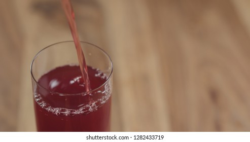 Closeup Pouring Cranberry Juice Into The Glass On Wood Table