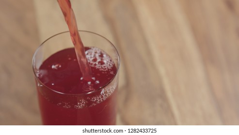 Closeup Pouring Cranberry Juice Into The Glass On Wood Table