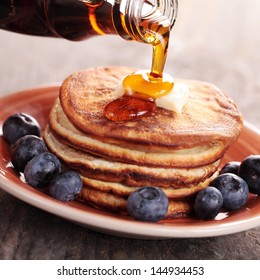 Close-up of pouring maple syrup on stack of pancakes.