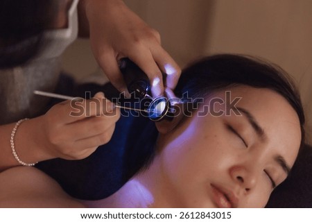 Close-up of practitioner inserting ear scoop into client’s ear canal during traditional ear cleaning therapy, focus on precision