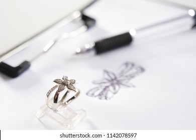 Close-up of a precious diamond ring depicting a flower; in the background we can see the drawing from which it was inspired. Concept of: wedding, luxury, jewelry.