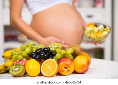 Close-up Of A Pregnant Belly With Fresh Fruit And Plate Of Salad. Healthy Pregnancy, Diet And Vitamins
