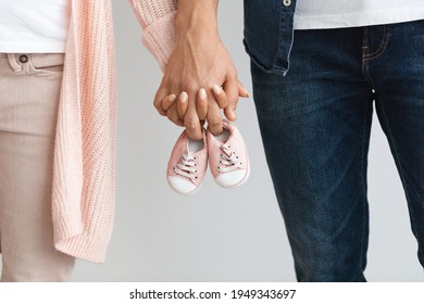Closeup of pregnant couple carrying small baby shoes while holding hands together, unrecognizable loving man and woman expecting baby, enjoying future parenthood, cropped image, free space - Shutterstock ID 1949343697