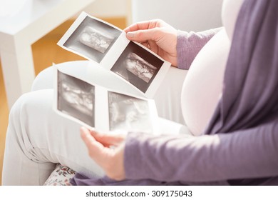 Close-up of pregnant woman holding ultrasound photos of fetus