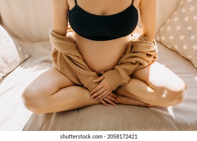 Closeup Of A Pregnant Woman Sitting On A Sofa In Soft Light, Wearing A Cozy Cardigan.