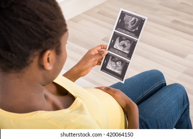 Close-up Of Pregnant Woman Sitting On Sofa Looking At Ultrasound Scan