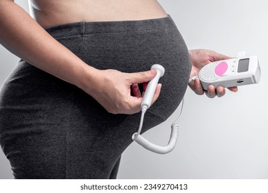 Close-up of pregnant woman using pocket fetal doppler to monitor baby heart beat at home, For baby healthcare with fetal doppler concept. - Shutterstock ID 2349270413