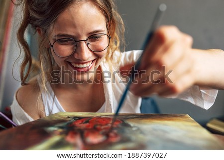 Closeup of a pretty female artist painting with a brush on canvas in her art studio. A woman painter with eyeglasses painting with oil searching for imagination in the workshop place.