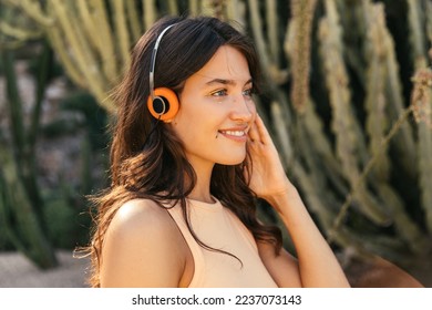 Close-up of pretty young caucasian girl looking at distance listens music in wireless headphones. Brunette wears light top. Concept of great mood, gadgets. - Powered by Shutterstock