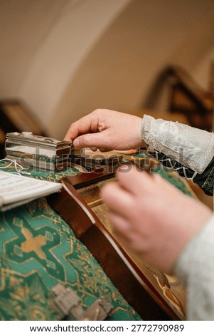 Close-up of a priest's hands reaching for a silver case with holy chrism on a green liturgical altar cover. Detail of an Orthodox baptism ceremony preparation.