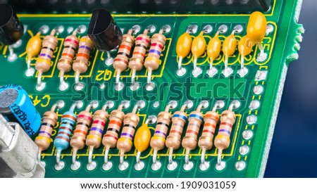 Closeup of printed circuit board with electronic components. Electrotechnics. Colorful resistors with standard color code, yellow or blue capacitors and black transistors on green PCB detail. E-waste.