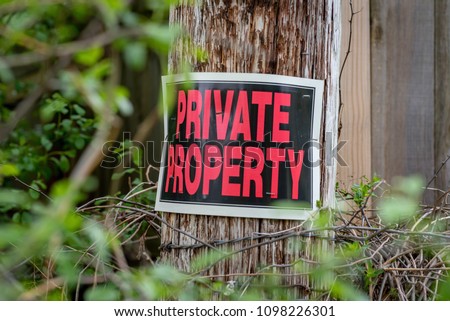closeup of a private property sign stapled to barbed wire post with thorns