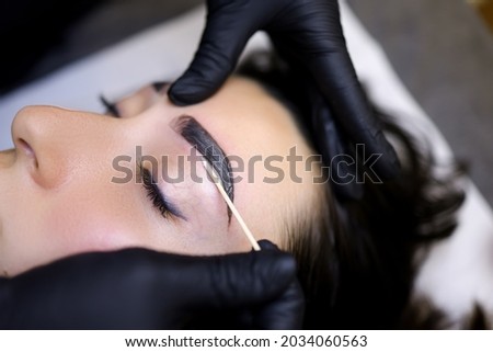 a close-up of the procedure of coloring the eyebrows with paint is performed after the procedure of lamination of the eyebrows
