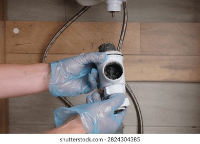Close-up of the process of dismantling and cleaning a plastic sink trap clogged with dirt and grease deposits.
