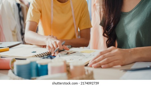 Close-up profession Asia lady designer teamwork meeting sketch book work on new collection share idea in shop. Young tailor discuss color for new cloth in workshop at table, Concept of collaboration. - Powered by Shutterstock