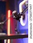 Closeup of professional adjustable studio microphone in neon podcast setup, ready for recording session. High quality audio production, voiceover, broadcasting concept. No people, blurred background