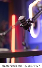 Closeup of professional adjustable studio microphone in neon podcast setup, ready for recording session. High quality audio production, voiceover, broadcasting concept. No people, blurred background