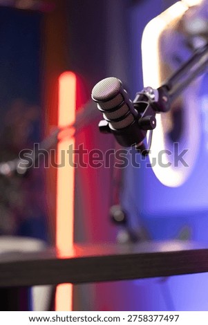 Closeup of professional adjustable studio microphone in neon podcast setup, ready for recording session. High quality audio production, voiceover, broadcasting concept. No people, blurred background