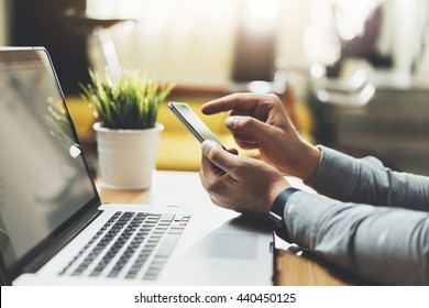 Close-up of professional businessman or lawyer using smartphone at modern office with vintage orange bicycle in the background, male designer or manager working via cellphone and laptop at new loft