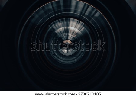 Close-up of professional camera lens front element with circular glass textures and light reflections,Macro shot looking directly into the glass of a professional photography lens, showing the intricate internal structure, aperture details, and concentric circular reflections in a dark, cinematic tone.