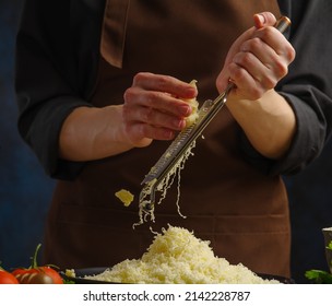 Close-up. A professional chef in a dark uniform grates cheese on a dark blue background. The concept is recipes for restaurant and home cooking dishes from cheese - pizza, pie, pasta, salad. - Powered by Shutterstock