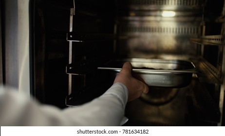 Closeup Of Professional Chef Man Put Meat Dish Into Oven At Restaurant Kitchen