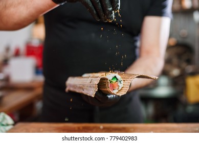Close-up of professional chef's hands in black gloves making sushi and rolls in a restaurant kitchen. Japanese traditional food. Preparation process.