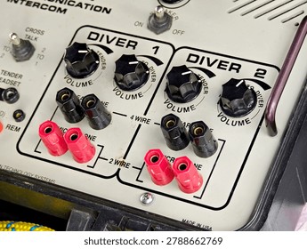 Close-up of professional diver communication intercom control panel with Diver 1 and Diver 2 volume knobs, red and black speaker terminals, toggle switches and 2 wire 4 wire connections, no people