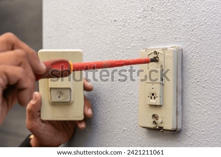 Close-up of a professional electrician's hand installing or fixing a wall mounted doorbell push button switch with a screwdriver.