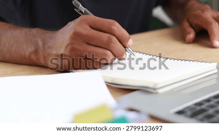 Close-up of a professional hand writing notes in a notebook beside a laptop at a modern workspace. Concept of planning, productivity, business strategy, education, project management, and organization.