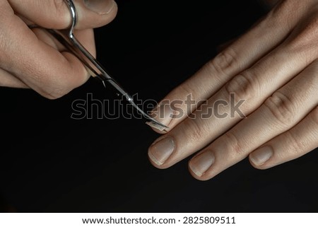 Close-up of professional hands using small scissors for careful nail trimming on black background. Ideal for beauty, manicure and personal care concepts