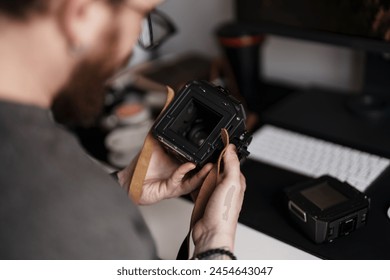 Close-up of a professional photographer carefully inspecting the details of a medium format camera against a modern office backdrop. - Powered by Shutterstock