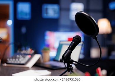 Closeup of a professional podcast microphone resting on a desk in a recording ready podcasting home studio. Selective focus of podcast equipment in empty room, ready to be used for online streaming