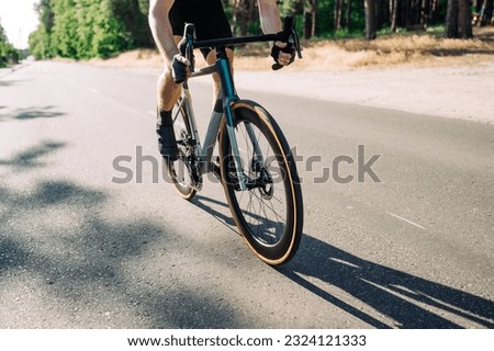 Close-up of a professional road bike and a man in gear riding it in the countryside against a forest background on a sunny day.