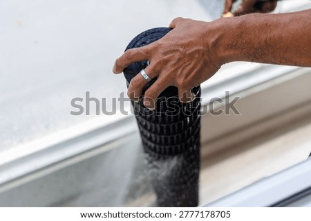 Close-up of professional technician hands using a high-pressure water sprayer to deep clean a dirty air conditioner blower wheel (fan blade) outdoors.