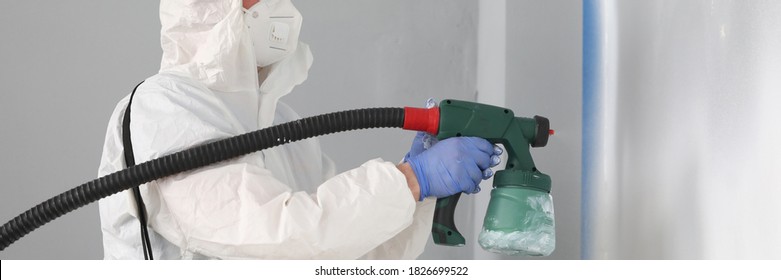 Close-up Of Professional Worker Painting Wall In Grey Colour With Spray Gun. Person In White Protective Costume And Face Mask. Renovation And Construction Site Concept