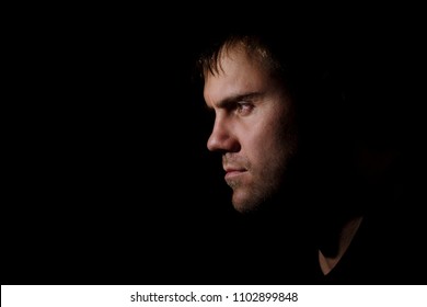 A Close-up Profile Portait Of A 30-35 Year Old Unshaven Man Looking Seriously And Thoughtfully Aside In The Dark. Portrait On The Black Background. Young Man's Toughts At Night.  Alone.