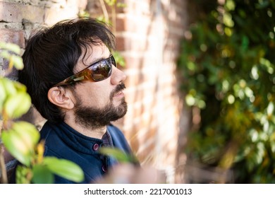 Close-up Profile Portrait Of A Latino Man On A Brick Wall Surrounded By Bushes