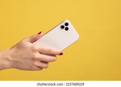 Closeup Profile Portrait Of Woman Hand Holding Mobile Phone, Showing Back Side Of Cell Phone. Indoor Studio Shot Isolated On Yellow Background.