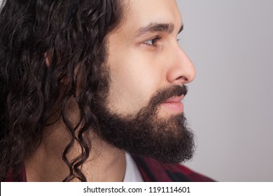 Closeup profile side view of handsome confident man with black long curly hair and beard, looking away with smile. male healthcare and beauty concept. indoor studio shot, isolated on gray background.