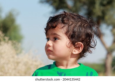 close-up profile view portrait of A small cute Indian Hindu child wearing a green shirt stands outside looking away