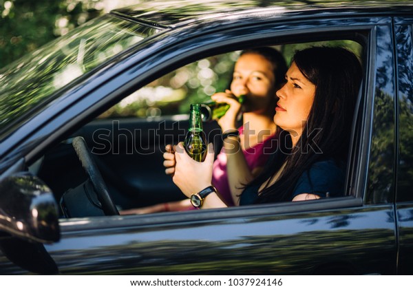 Closeup profile of\
woman driver holding a beer while sitting on the front sear while\
her friend is drinking one\
