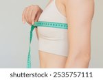 Close-up profile of young pretty Caucasian brunette woman in beige underwear measuring her chest circumference with a green centimeter tape.