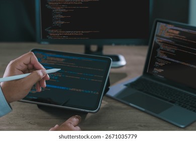 Close-up of programmer freelance working on tablet and laptop with code on screen, modern software development, coding, and remote work in home office environment.