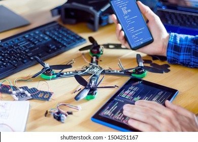 Closeup programmer hand holding smartphone and tablet with program code of software on screen for controlling FPV - first person view drone. Building quadcopter from kit with microcontrollers.