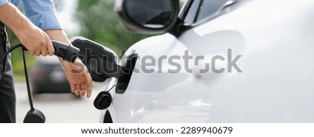 Closeup progressive man holding EV charger plug from public charging station for electric vehicle with background of residential building as concept eco-friendly sustainability energy car concept.