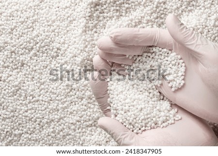 Close-up of a protectively gloved hand holding a lot of white plastic polymer granules. Industrial background for advertising and photography.